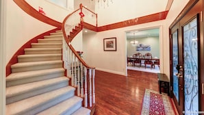 A grand staircase with a chandelier, wooden walls, and a dining area with a chandelier.
