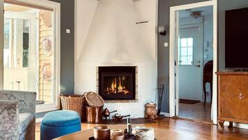 Una sala de estar con chimenea, un reposapiés azul, una mesa de centro redonda con juegos de té y un aparador de madera.