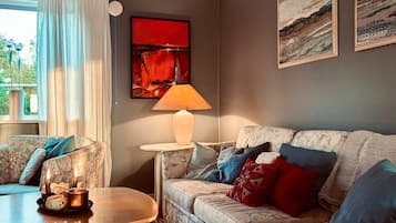 Una sala de estar con un sofá, una mesa con velas, una lámpara y obras de arte en la pared.
