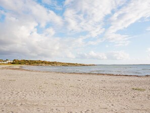 A beach with a sandy shore, calm water, and a distant shoreline with vegetation and a wind turbine. - 4 Star Holiday Home in Varberg-by Traum (Varberg)