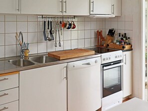 A kitchen with white cabinets, a stainless steel sink, a wooden cutting board, a dishwasher, and an oven. - 4 Star Holiday Home in Varberg (Varberg)