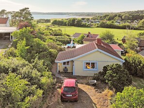 Una casa con un coche rojo estacionado frente, rodeada de vegetación y con vista al mar.
