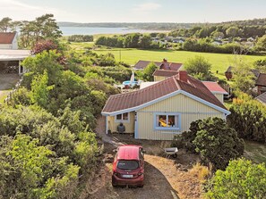 Ein eingeschossiges Haus mit rotem Dach, umgeben von üppiger Vegetation und Blick auf einen See.