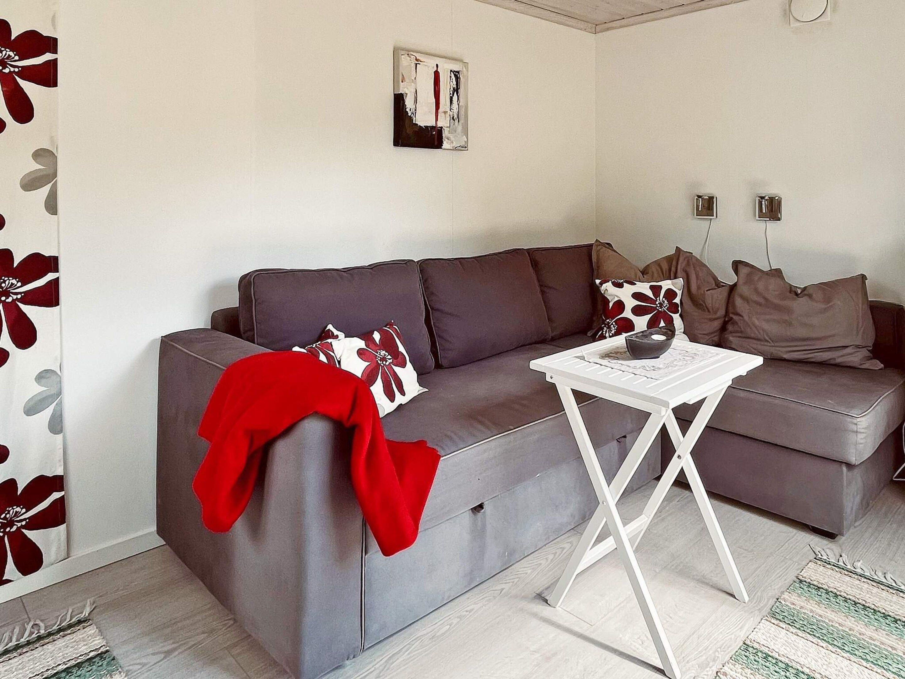Un salon avec un canapé gris, une table basse blanche et un plaid rouge.