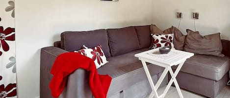 Una sala de estar con un sofá gris, una mesita de centro blanca y una manta roja.