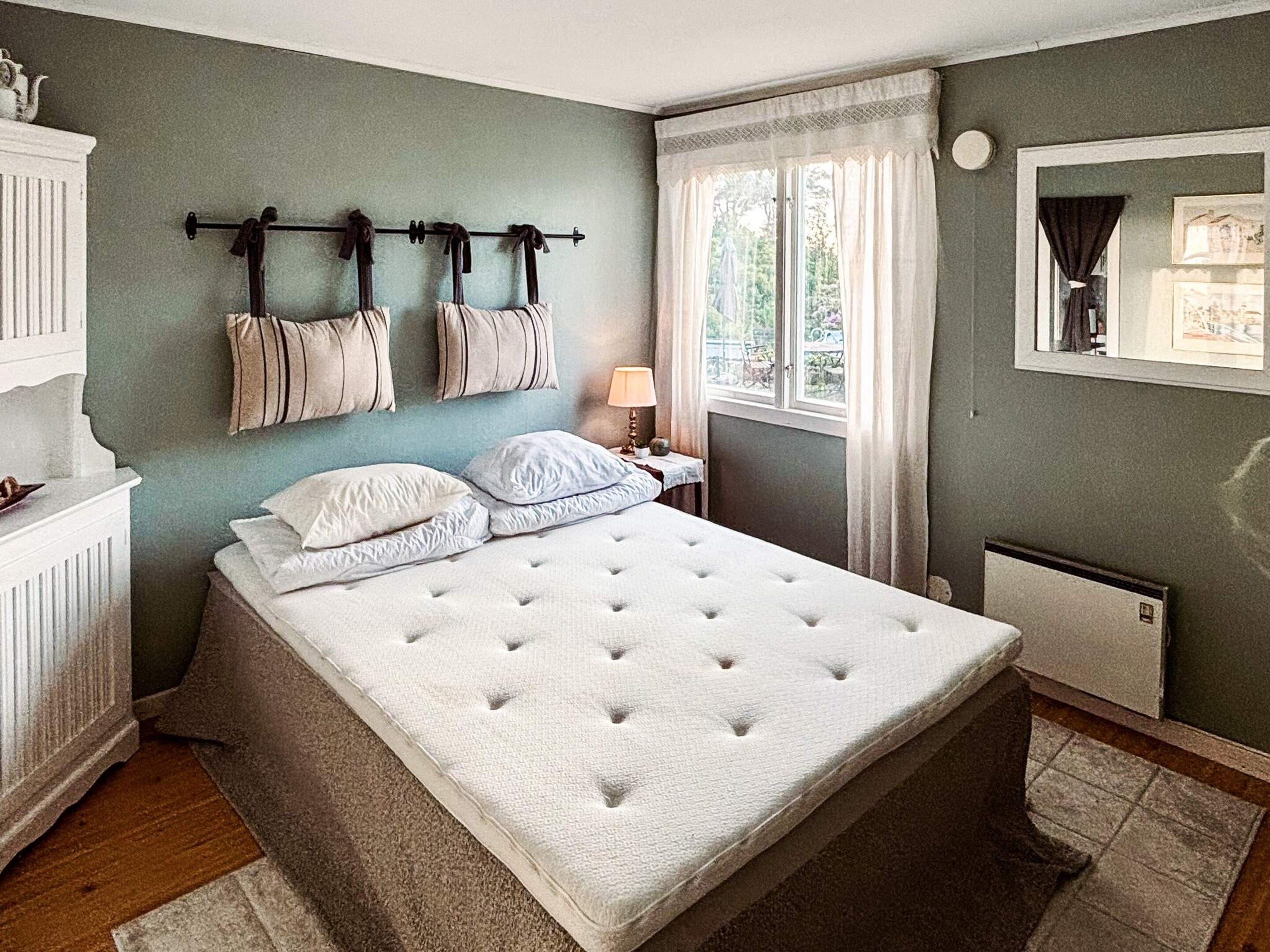 Un dormitorio con una cama grande, un radiador, una ventana con cortinas y un perchero en la pared.
