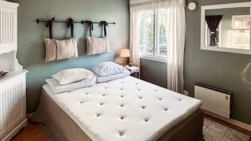 Un dormitorio con una cama grande, un radiador, una ventana con cortinas y un perchero en la pared.