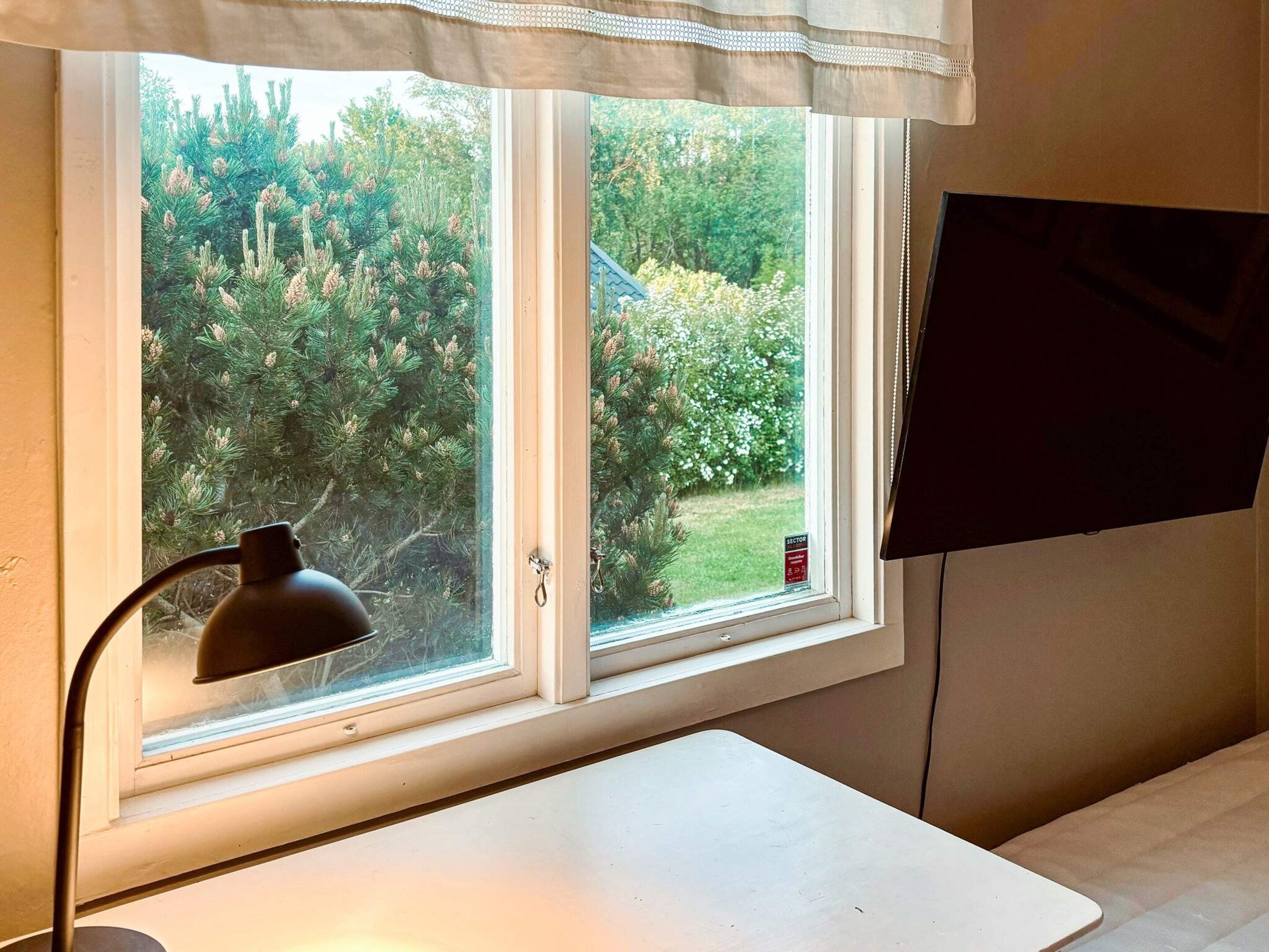 Ein Zimmer mit Fenster, Schreibtisch, Lampe und Fernseher.