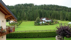 Una casa a due piani con un balcone, circondata da un prato curato e da montagne boscose sullo sfondo.