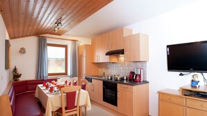 Una cucina compatta con mobili in legno, una zona pranzo con una panca rossa e un televisore fissato al muro.