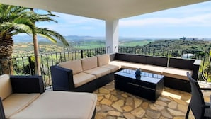 A balcony with a stone floor, a sofa, a coffee table, and a view of a hilly landscape. - >>casa Conil Buena Vista<< (Conil de la Frontera)