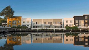 Una hilera de edificios modernos con balcones, reflejados en agua tranquila.