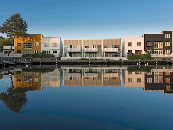 A row of modern buildings with balconies, reflecting in calm water.