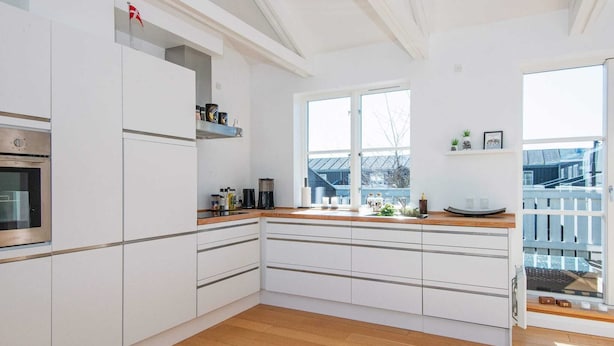Una cocina moderna con armarios blancos, horno empotrado y un ventanal que proporciona luz natural.
