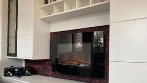 Un soggiorno con una TV a schermo piatto montata a parete, un mobile bianco sottostante e una parete di fondo con motivo rosso.