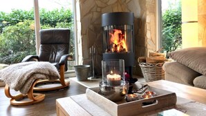 Un salon chaleureux avec un mur en pierre, un fauteuil en cuir noir, un fauteuil à bascule en bois, une table avec une bougie et une cheminée.