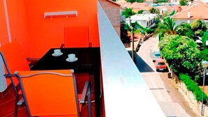 A balcony with a table and chairs, overlooking a street with houses and greenery. - Apartments St Rialto - Comfort One-bedroom Apartment With Balcony and Sea View (Jelsa)