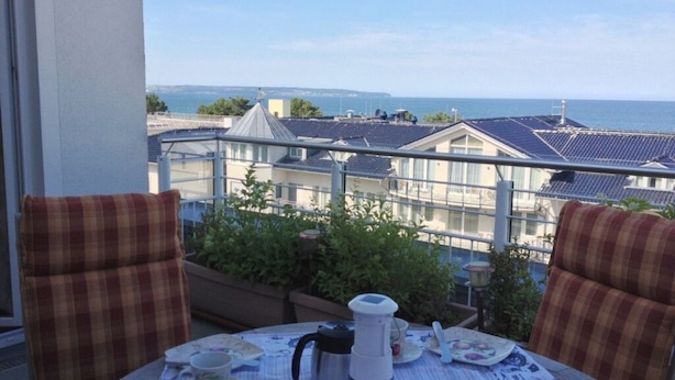 A balcony with a table set for tea, overlooking a residential area with houses and a view of the sea. - 55, Apartment House "bel-vital" (Binz)