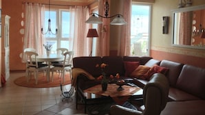 A cozy living room with a brown leather sofa, a coffee table with flowers, a dining table with chairs, and a large window with curtains. - 55, Apartment House "bel-vital" (Binz)