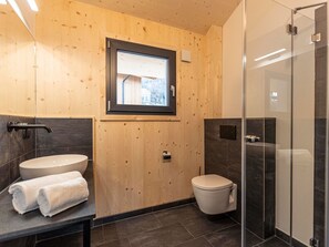 A modern bathroom with a wooden wall, a window, a sink, a toilet, and a glass shower enclosure.