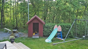 A wooden deck, a small red shed, a green slide, and a swing set in a wooded area. - 11 Person Holiday Home in Gjesdal-by Traum (Gjesdal)