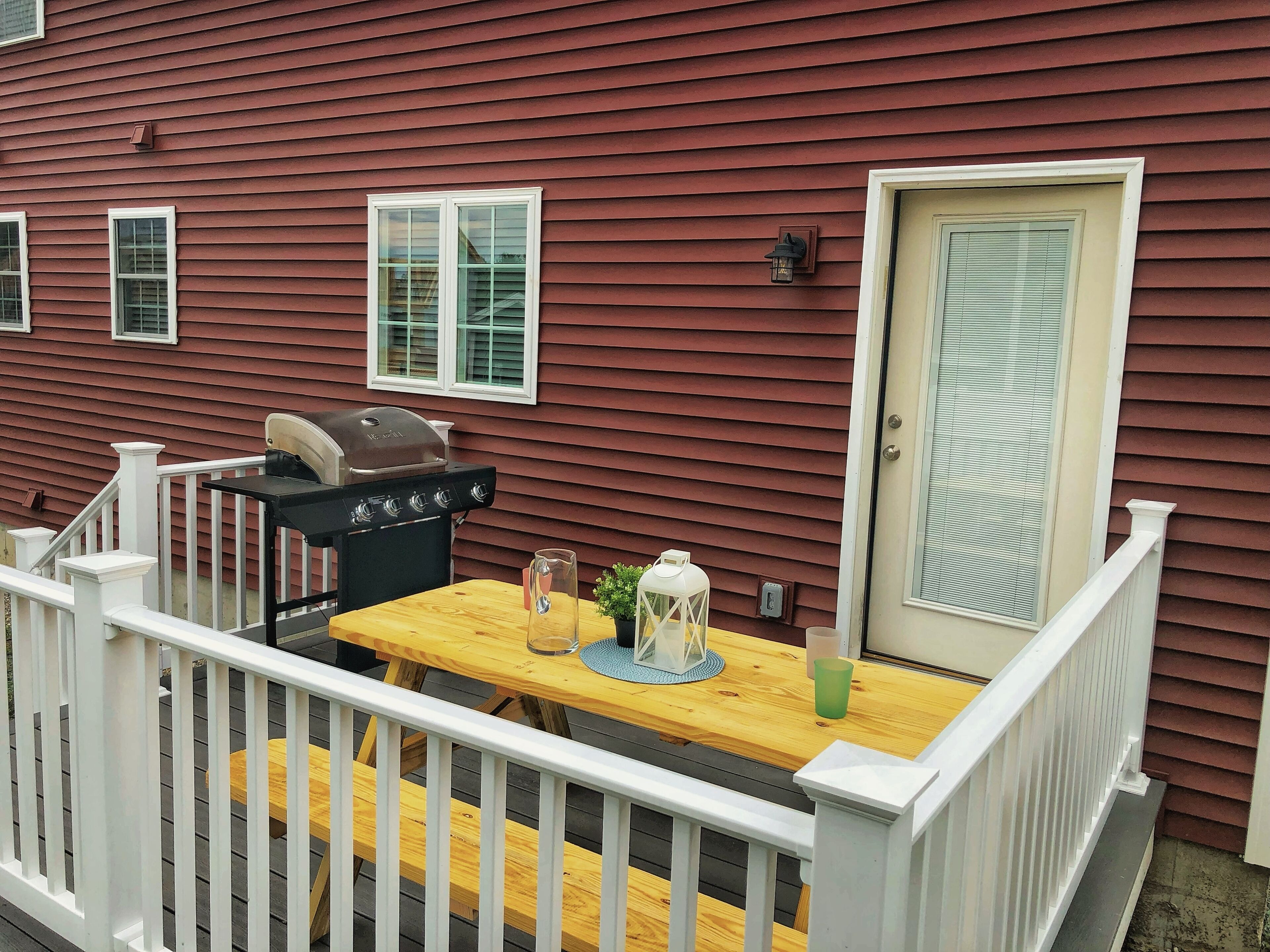 A wooden deck with a grill, a table with a glass, and a door with a window.
