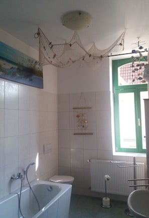 Un bagno con vasca, servizi igienici e una finestra con stipite verde.