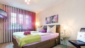 A modern bedroom with a large bed, a bedside table, a chair, and a window with curtains.