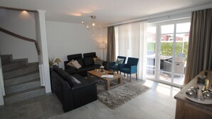 A modern living room with a staircase, a sofa set, a coffee table, and a dining area with a view of the outdoors. - Residence Island Pearl (Langeoog)