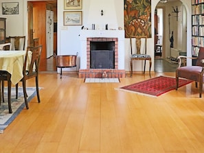 A living room with a fireplace, wooden flooring, a dining table, chairs, a red rug, and a bookshelf. - 4 Star Holiday Home in Langaryd (Långaryd)