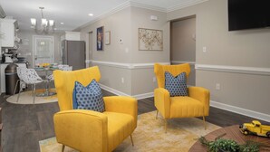 A modern living room with two yellow armchairs, a dining area, a kitchen, and a mounted TV. - Modern Home In PRIME location - King Bed/ Spacious

 (Rocky Mount)