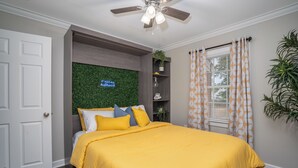A bedroom with a bed, a ceiling fan, a green wall, a window with patterned curtains, and a door. - Modern Home In PRIME location - King Bed/ Spacious

 (Rocky Mount)