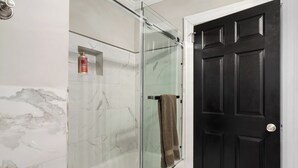 A bathroom with a glass shower enclosure, marble tiles, a black door, and a towel hanging on the shower door.