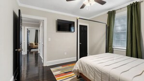 A bedroom with a bed, a ceiling fan, a TV, and a window with curtains.