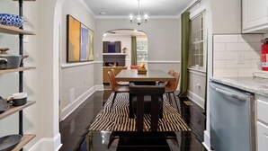 A modern kitchen with a built-in oven, a dining area with a black and white patterned rug, and a hallway leading to a living space.