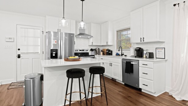 A modern kitchen with white cabinetry, stainless steel appliances, and two bar stools.