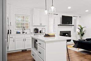 A modern kitchen with white cabinetry, a central island, and a black sofa in the living area.