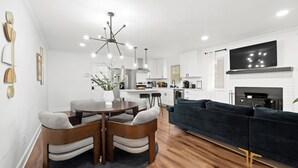 A modern living room with a dark blue sofa, wooden dining table with chairs, and a kitchen in the background.