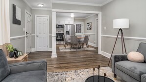 Un salon moderne avec un canapé gris, une table basse et un lampadaire. On aperçoit à l’arrière-plan un coin repas avec une table et des chaises.