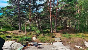 A wooden deck leading into a forested area with a grill and pots on the ground. - 7 Person Holiday Home in Vesteroy-by Traum (Hvaler)