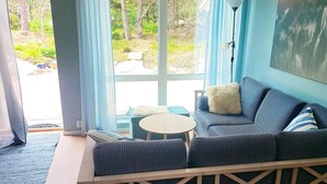 A cozy room with a blue sofa, a small round table, and a view of a garden through large windows. - 7 Person Holiday Home in Vesteroy-by Traum (Hvaler)
