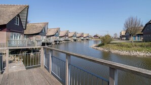 Een houten looppad dat naar een rij rieten huizen aan een rustige rivier leidt.
