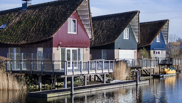 Een rij met rieten daken, met een steiger die uitsteekt in een kalm waterlichaam.