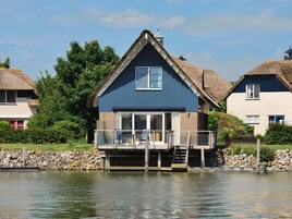 Ein Haus mit Balkon, einem Reetdach und Blick auf das Wasser.