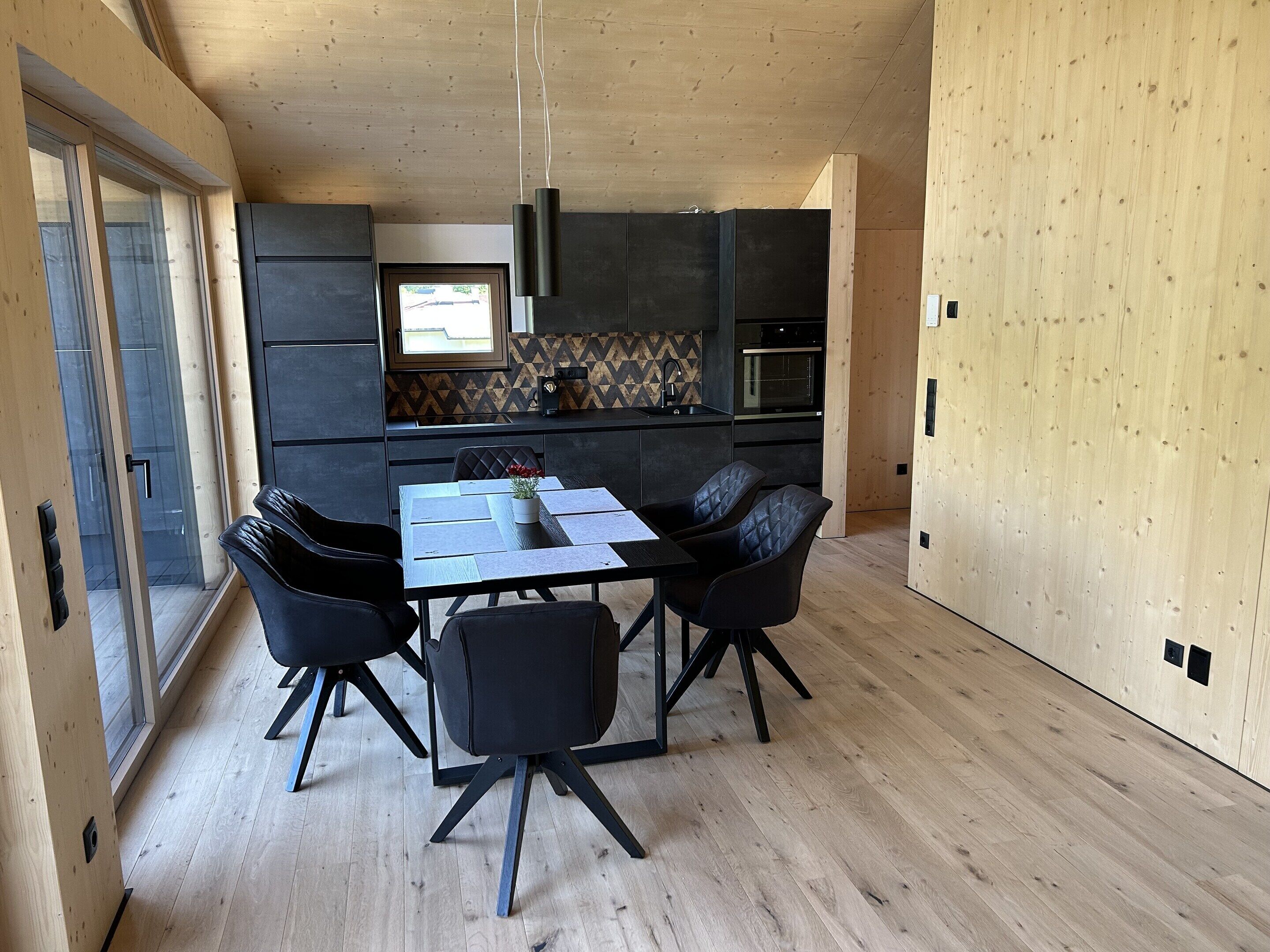 A modern kitchen with dark cabinets, a central island, and a window overlooking the street.