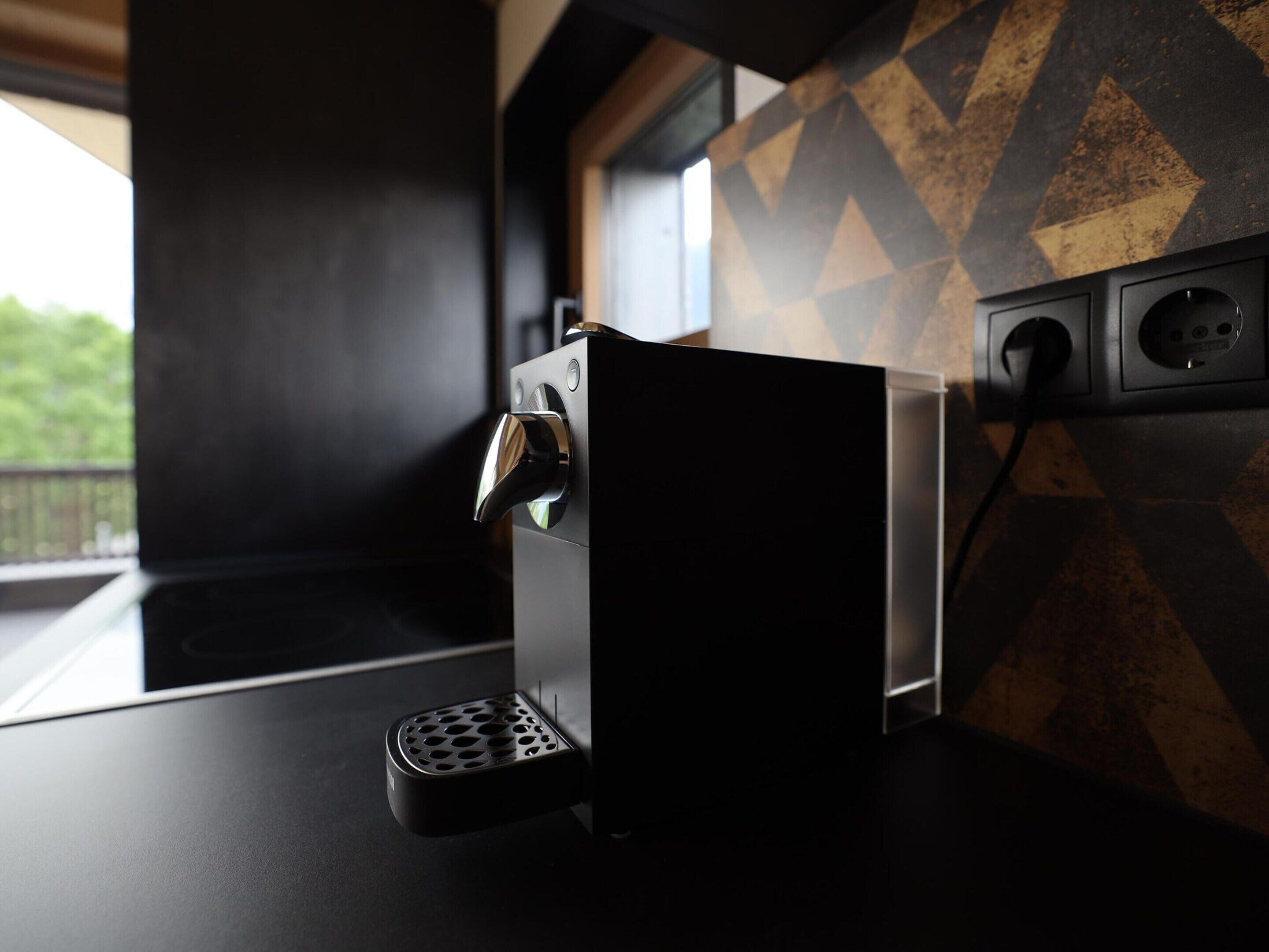 Une cuisine moderne dotée d’une machine à expresso intégrée, d’un plan de travail noir et d’un crédence au motif géométrique.