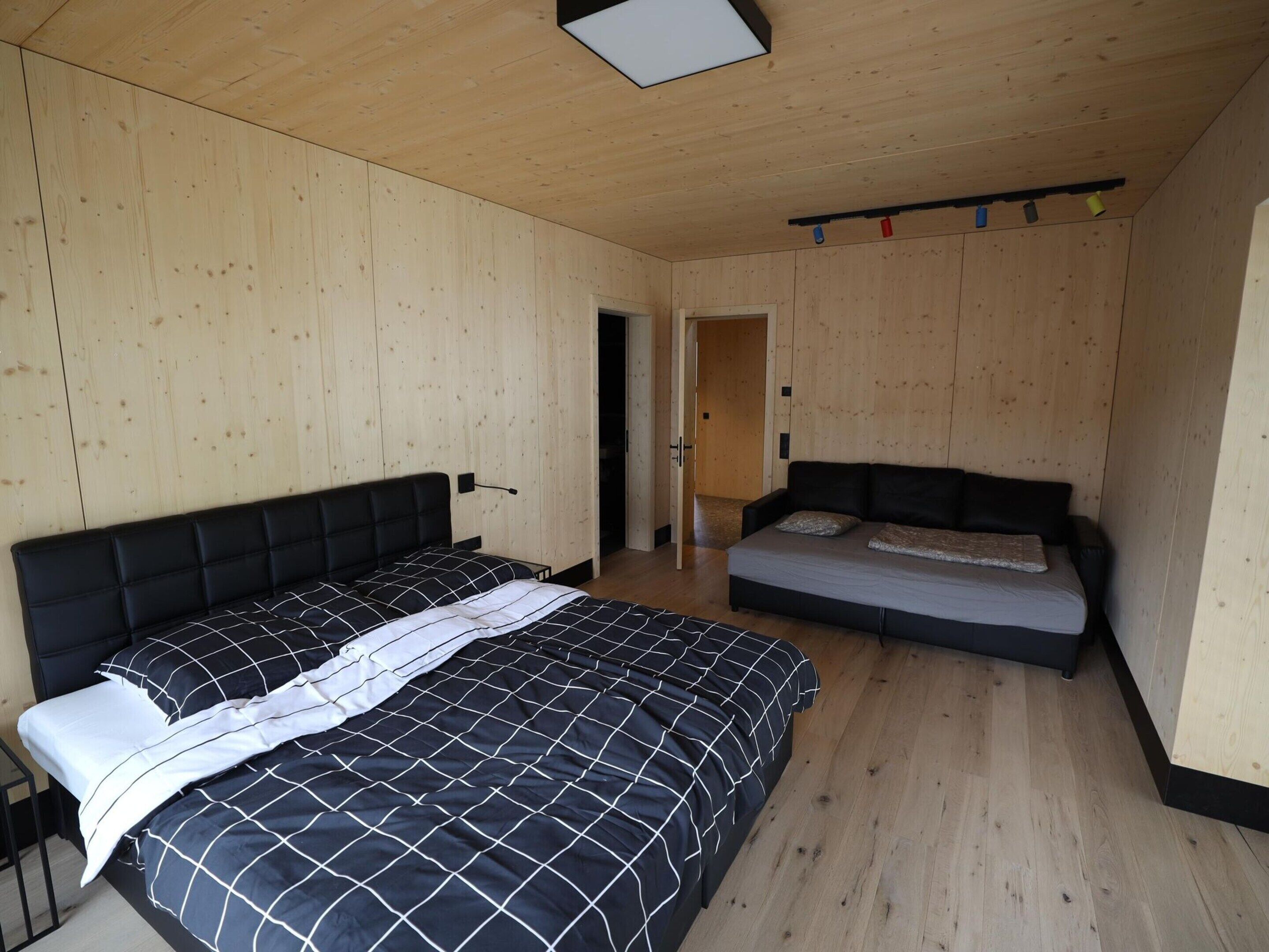 A bedroom with a bed, a sofa, wooden walls, and a ceiling light fixture.