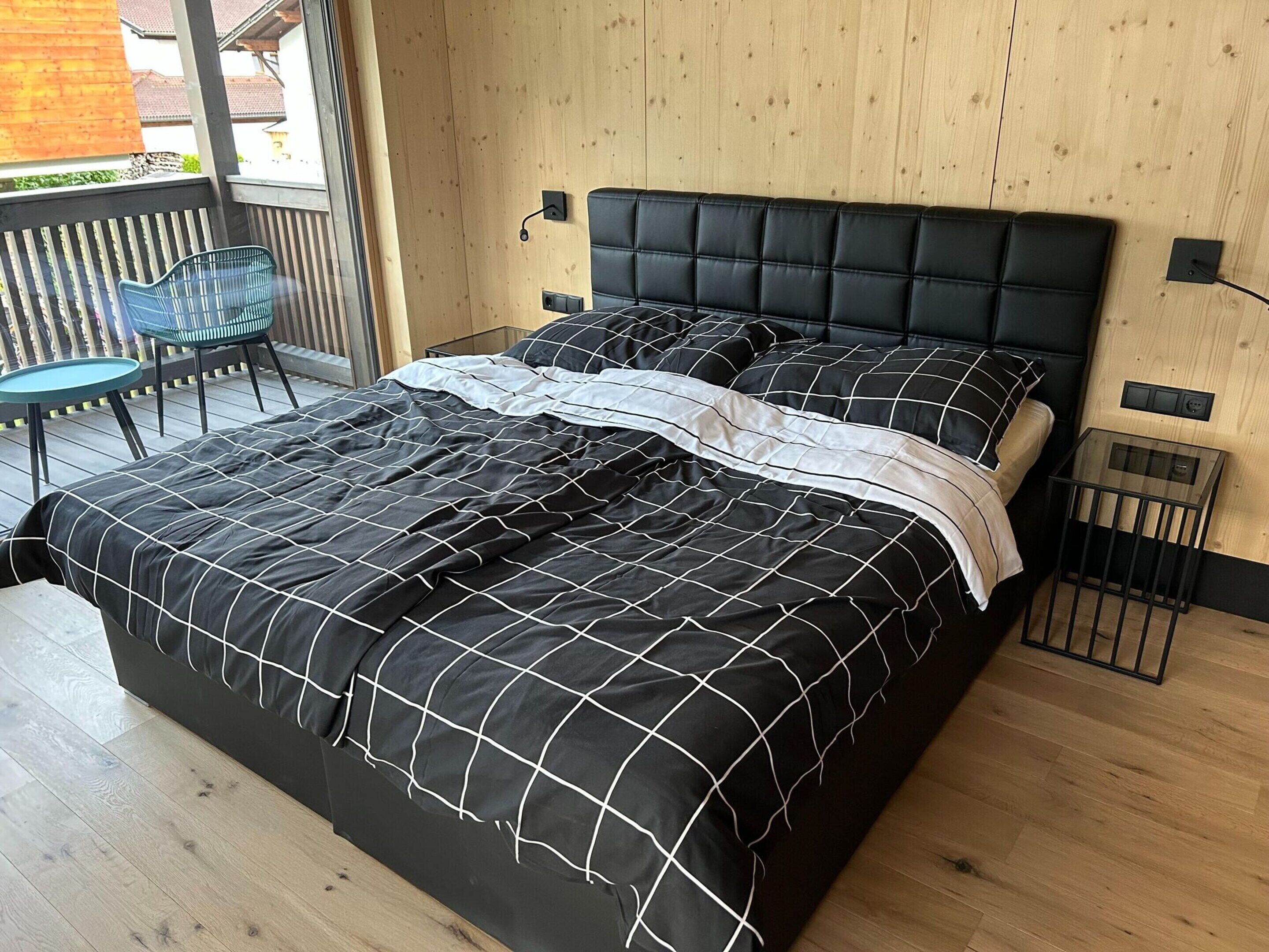A modern bedroom with a black and white checkered bedspread, a tufted headboard, and a small glass table beside the bed.