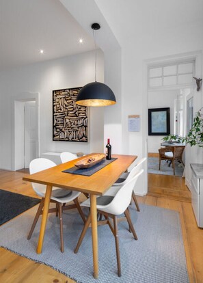 A dining area with a wooden table, white chairs, a black pendant light, and a stone wall art piece. - in het Blauwe Huis - BG (Garmisch-Partenkirchen)