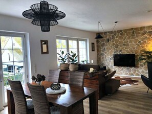 A spacious living area with a stone wall, a dining table with chairs, a sofa, and a TV mounted on the wall. - Moselle-side Apartments (Mehring)